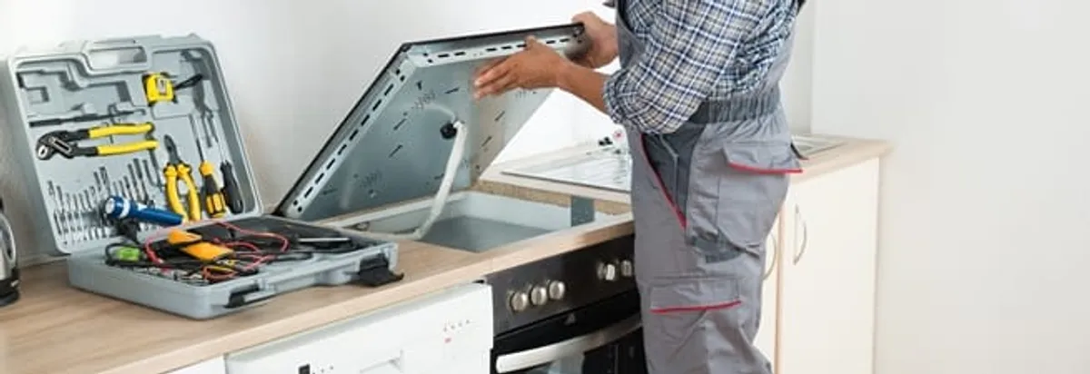 Cooktop repair technician lifting a built-in stovetop for service in Fort Worth, TX